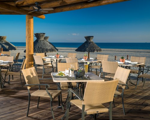 AN OUTDOOR DINING AREA WITH THATCHED SUNSHADES ALONGSIDE THE BEACH.