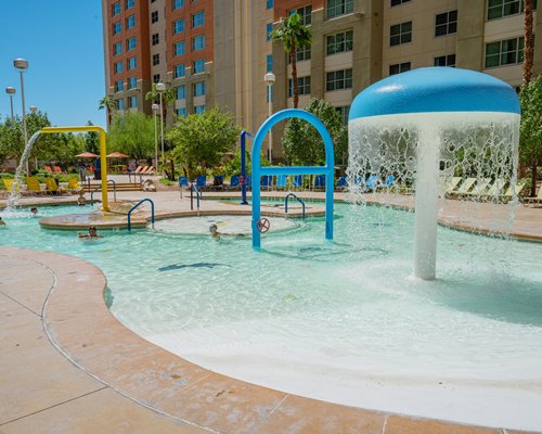 An outdoor swimming pool with chaise lounge chairs patio and sunshades alongside multi story units.