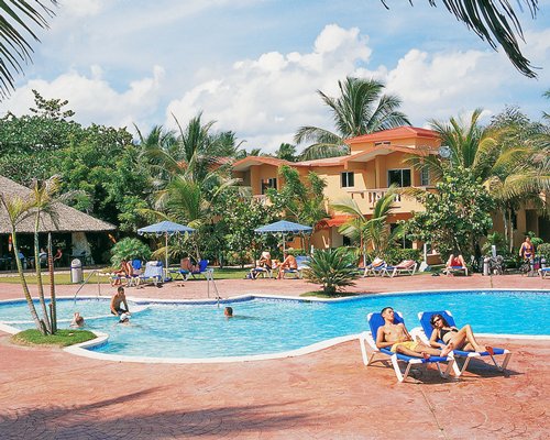 An outdoor swimming pool with sunshades and chaise lounge chairs alongside the resort.