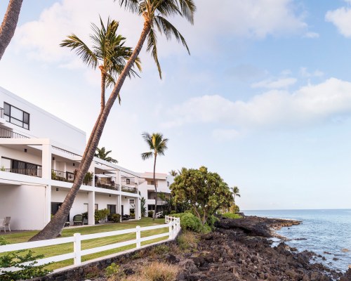 A VIEW OF MULTI STORY RESORT UNITS WITH TREES FACING THE OCEAN.