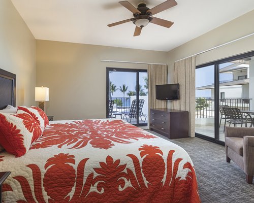 A well furnished bedroom with television alongside patio furniture and chaise lounge chairs in the patio.