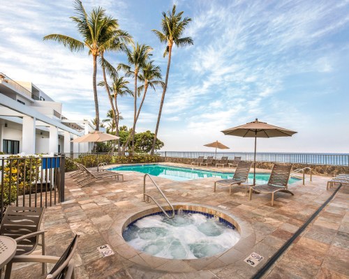 AN OUTDOOR SWIMMING POOL WITH CHAISE LOUNGE CHAIRS SUNSHADES ALONGSIDE A HOT TUB.