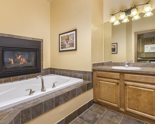 A bathtub with a fire in the fireplace and single sink vanity.
