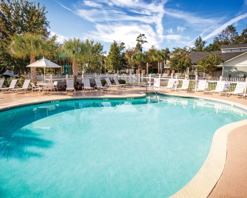 AN OUTDOOR POOL WITH CHAISE LOUNGE CHAIRS AND LANDSCAPED EXTERIOR.
