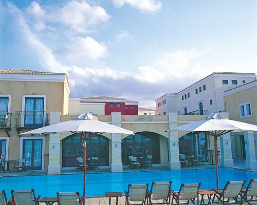 Exterior view of Plaza Spa Apartments with outdoor swimming pool chaise lounge chairs and sunshades.