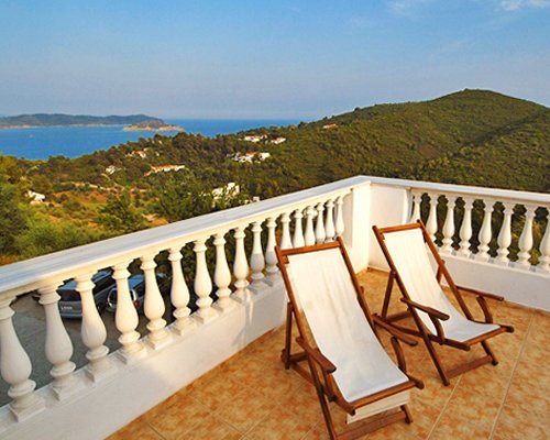 A balcony with chaise lounge chairs alongside the mountains and the sea.