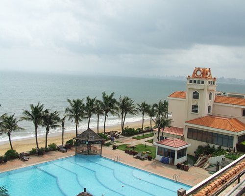 Balcony view of an outdoor swimming pool with trees alongside the sea.