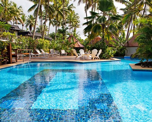 A large outdoor swimming pool with chaise lounge chairs patio furniture and trees alongside resort units.