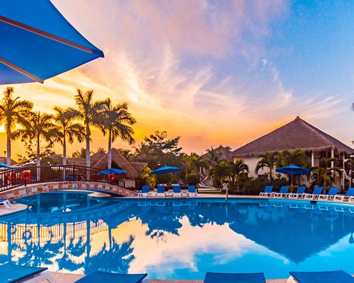 A landscaped outdoor swimming pool with bridge chaise lounge chairs and sunset view.