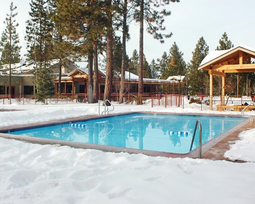 An outdoor swimming pool with trees alongside resort units covered in snow.