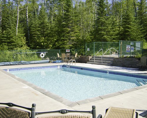 Outdoor swimming pool with chaise lounge chairs surrounded by wooded area.