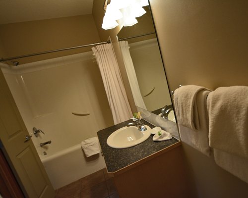 A bathroom with bathtub shower and a single sink vanity.