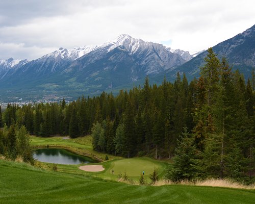 Golf course with the waterfront alongside the wooded area and mountains.
