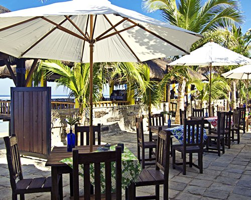 An outdoor restaurant with patio tables and sunshades surrounded by trees.