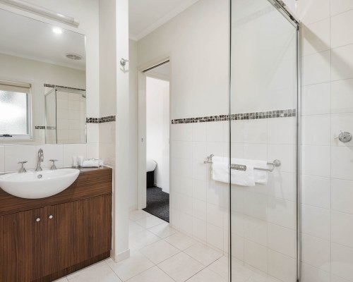 A BATHROOM WITH SHOWER AND SINGLE SINK VANITY ALONGSIDE BEDROOM.