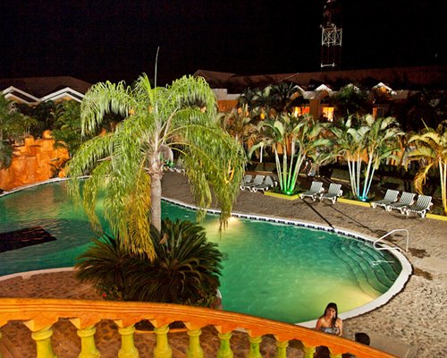 An outdoor swimming pool and chaise lounge chairs with trees at night.