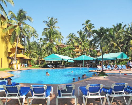A large outdoor swimming pool with chaise lounge chairs and trees alongside multi story resort units.