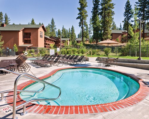 An outdoor hot tub with chaise lounge chairs alongside the resort with the pine trees.