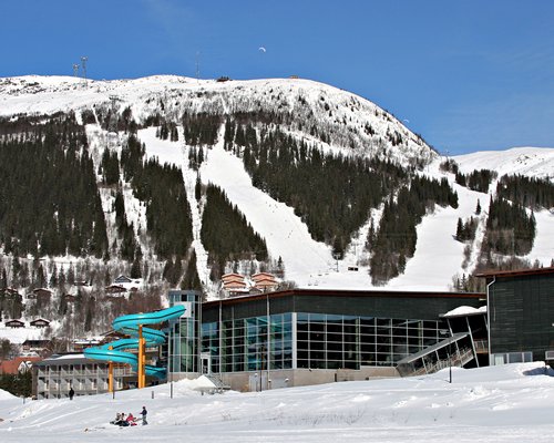 Exterior view of Holiday Club Are with a slide alongside the mountains and wooded area during winter.