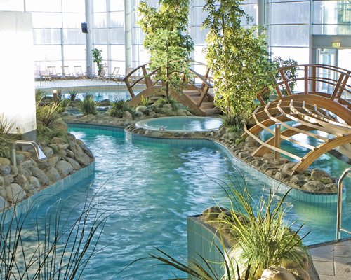 A bridge over an indoor swimming pool with hot tub and an outside view.