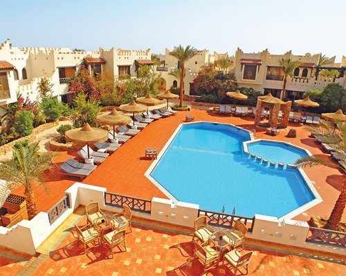 An outdoor swimming pool with hot tub and chaise lounge chairs alongside multi story resort units.