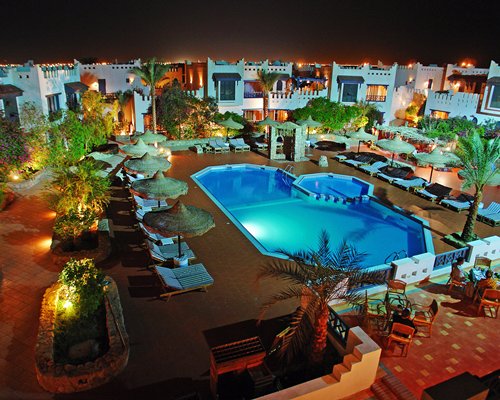 An outdoor swimming pool with chaise lounge chairs and thatched sunshades.