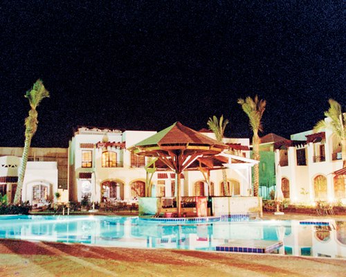An outdoor swimming pool alongside multi story resort units at night.