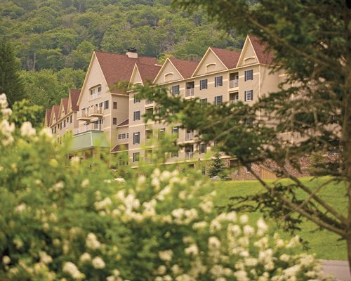 An exterior view of multi story resort units with flowering shrubs surrounded by wooded area.