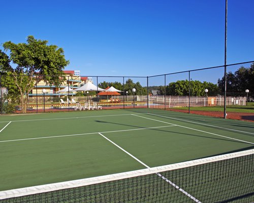 An outdoor tennis court with trees alongside the swimming pool.