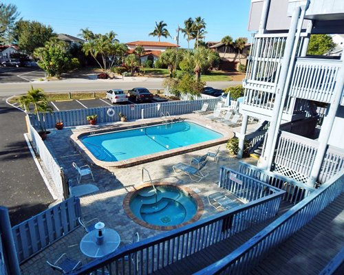 An outdoor pool and hot tub with chaise lounge and patio chairs alongside a parking lot.