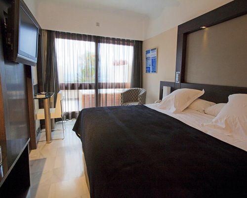 A well furnished bedroom with a king bed television and an outside view.