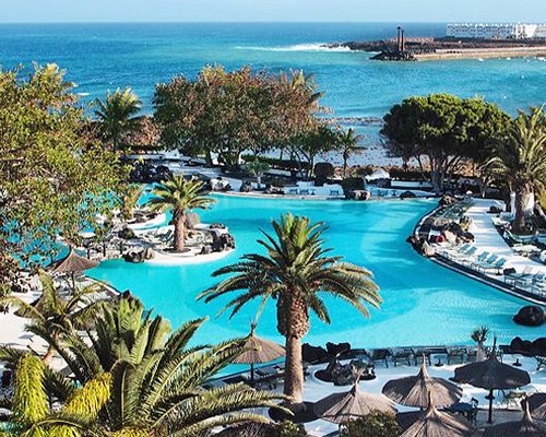 Outdoor swimming pool with chaise lounge chairs and sunshades alongside the beach.