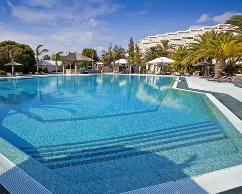Large outdoor swimming pool with sunshades and palm trees.