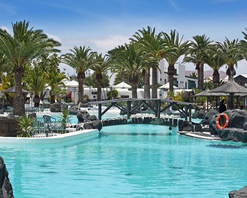 Large outdoor swimming pool with sunshades bridge and palm trees.
