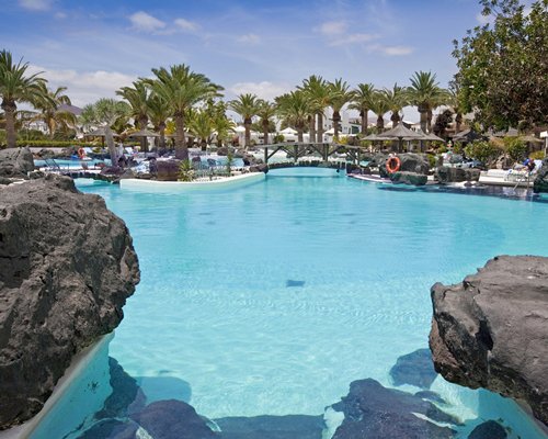 An outdoor swimming pool with chaise lounge chairs and thatched sunshades.