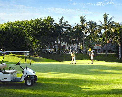 Two people playing in a well maintained golf course alongside a golf cart.