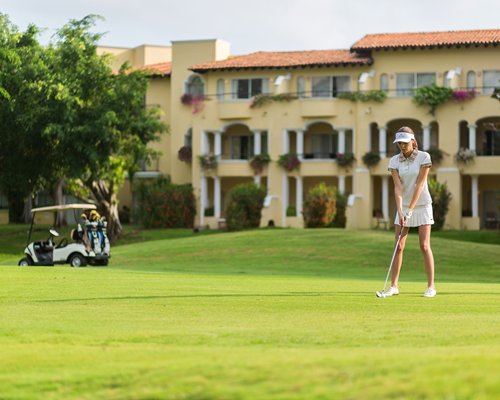 A golf cart and a golfer playing golf at the golf course alongside multiple balconies.
