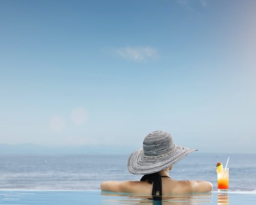 A woman with a beverage at a swimming pool alongside the beach.