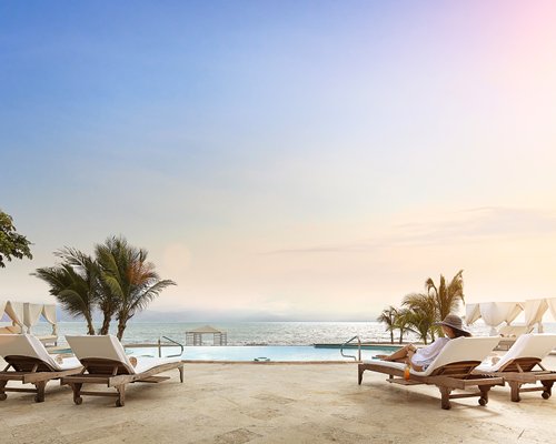 A lady sitting on the chaise lounge chair facing the ocean.