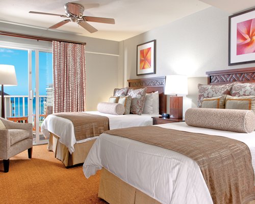 A well furnished bedroom with two beds balcony and ocean view.