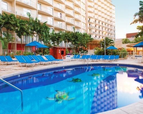 An outdoor swimming pool with a chaise lounge chairs and sunshades alongside the resort.