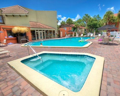 Outdoor swimming pool and hot tub with chaise lounge chairs and dining with sunshade alongside a unit.