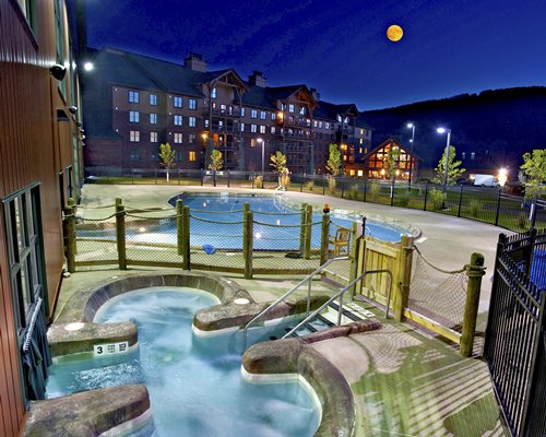 An outdoor hot tub and swimming pool alongside the resort at night.