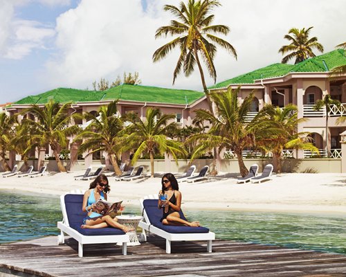 Grand Colony Island Villas alongside the beach with palm trees and women in chaise lounge chairs on a wooden pier.
