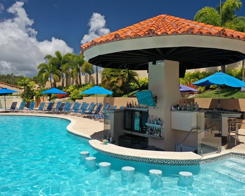An aerial view of an outdoor swimming pool with chaise lounge chairs and sunshades alongside the unit.