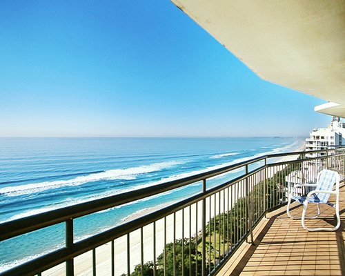 View of the beach and sea from balcony with patio chair.