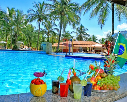 Outdoor swimming pool with fountain  and beverages at a bar counter of the poolside bar surrounded by palm trees.
