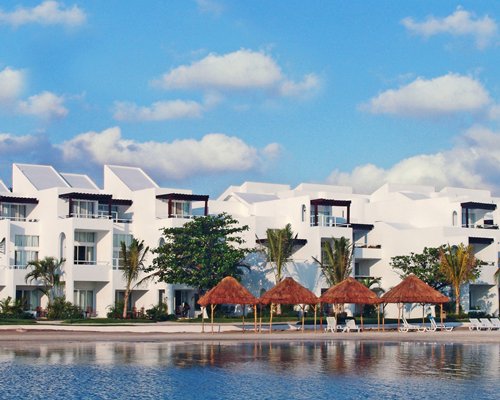 An exterior view of the resort with chaise lounge chairs and thatched sunshades alongside the waterfront.