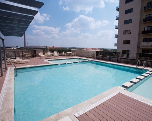 An outdoor swimming pool with chaise lounge chairs alongside multi story units.