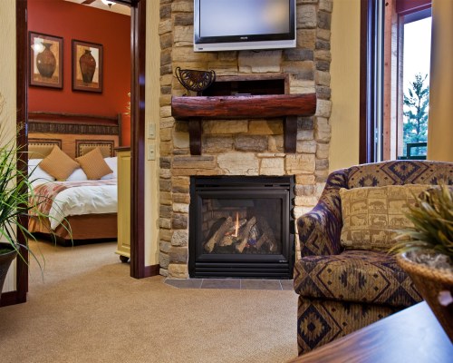A WELL FURNISHED LIVING ROOM WITH TELEVISION AND FIREPLACE ALONGSIDE BEDROOM.